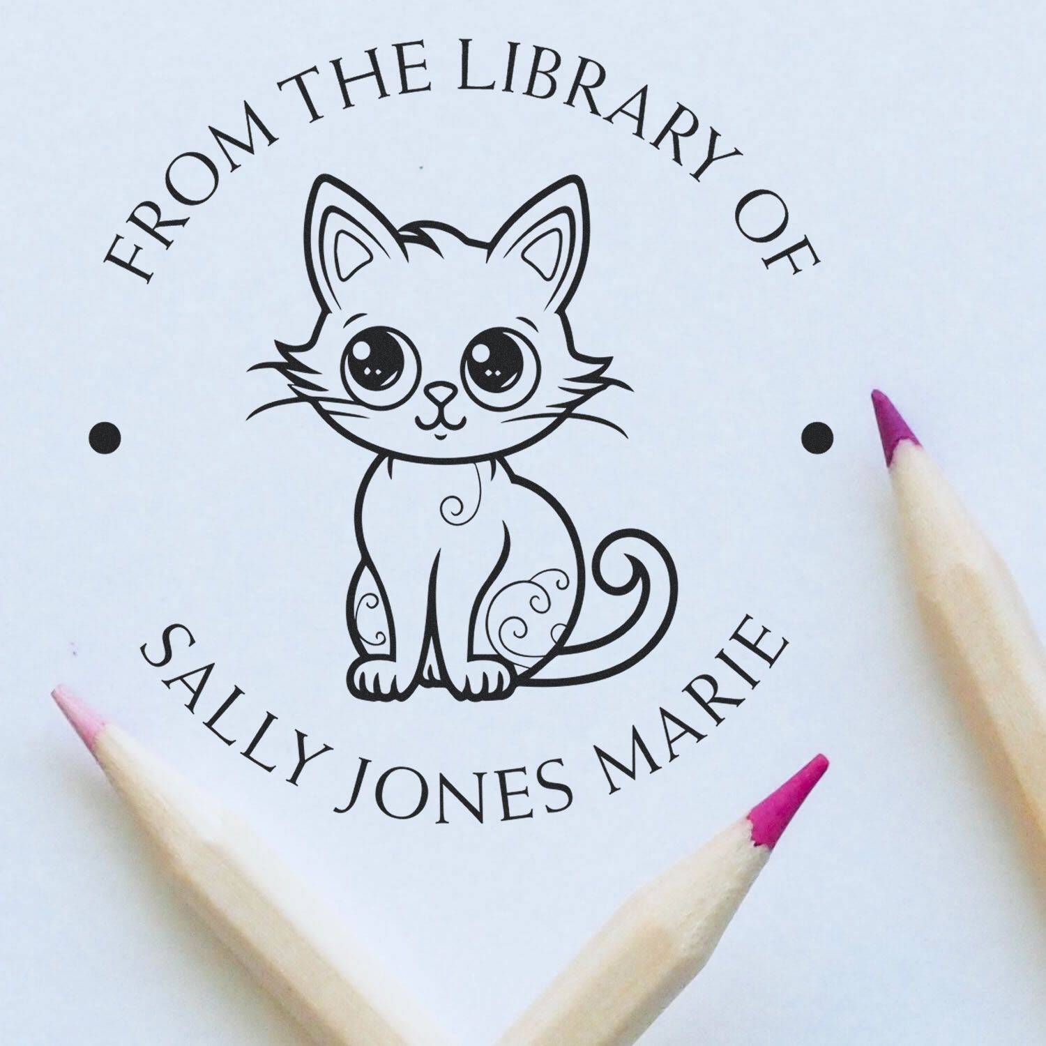 Black personalized cat library stamp seal with curved text on white paper, framed by pink-tipped pencils.
