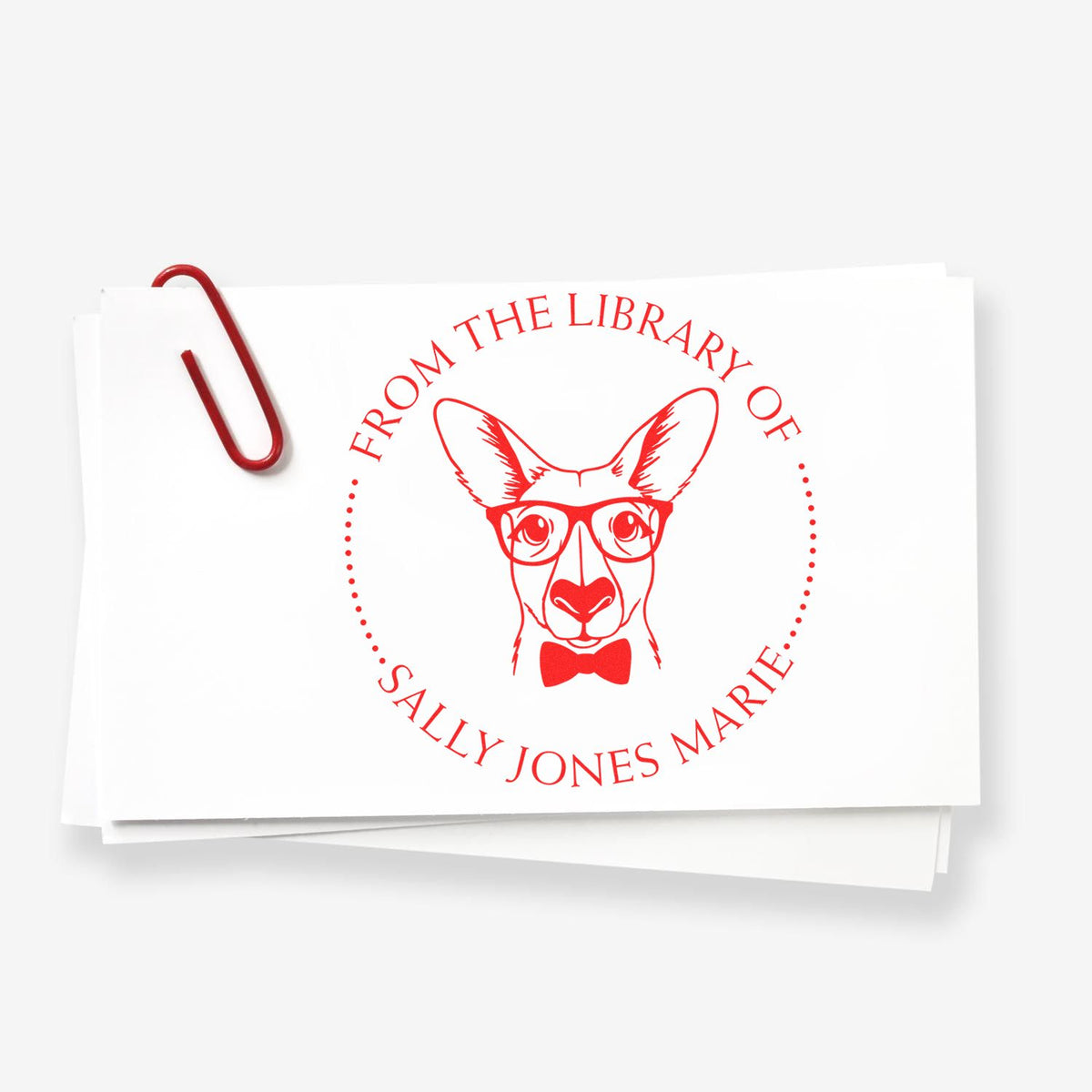 Red custom library stamp seal with glasses-wearing dog and bow tie on white paper, clipped with a red paperclip.