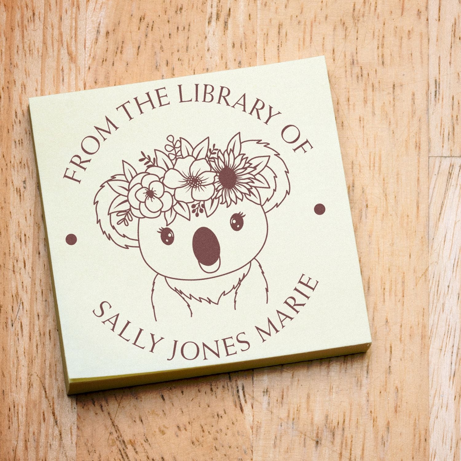 Cream custom stamp seal with burgundy koala, floral crown, and circular name text on a wood background.