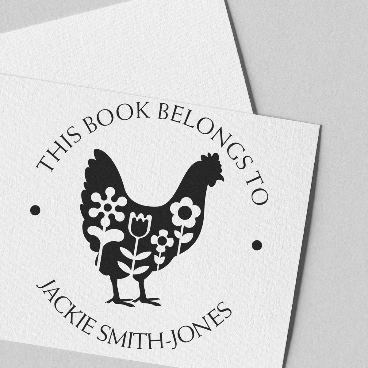 Black chicken floral bookplate stamp seal on white textured paper, reading This Book Belongs to Jackie Smith-Jones.