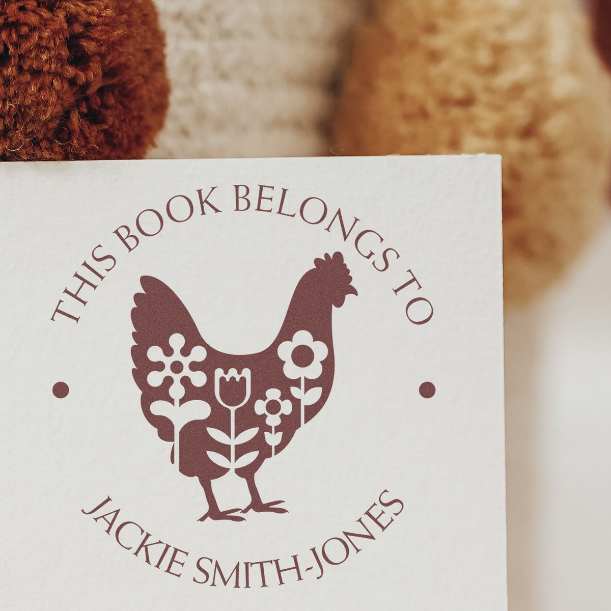 Maroon personalized book stamp seal with chicken and flowers on white card, reading This Book Belongs To Jackie Smith-Jones
