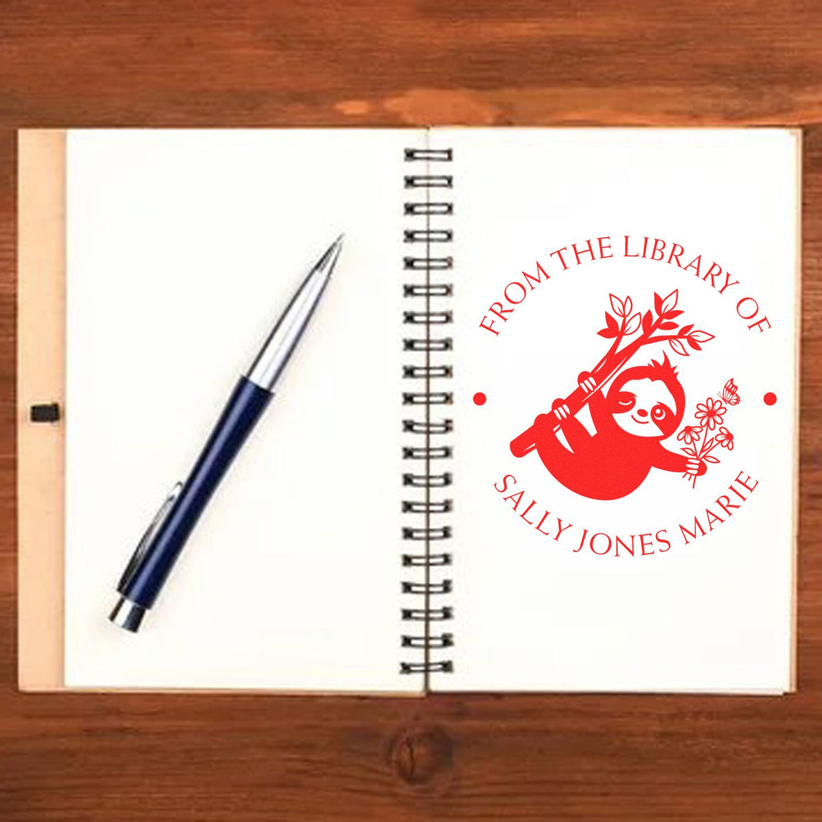 Red custom library stamp seal on an open spiral notebook, with a blue pen on white pages.