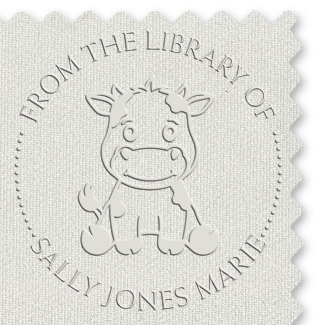 White embossed stamp seal with cartoon cow and circular text From the Library of Sally Jones Marie
