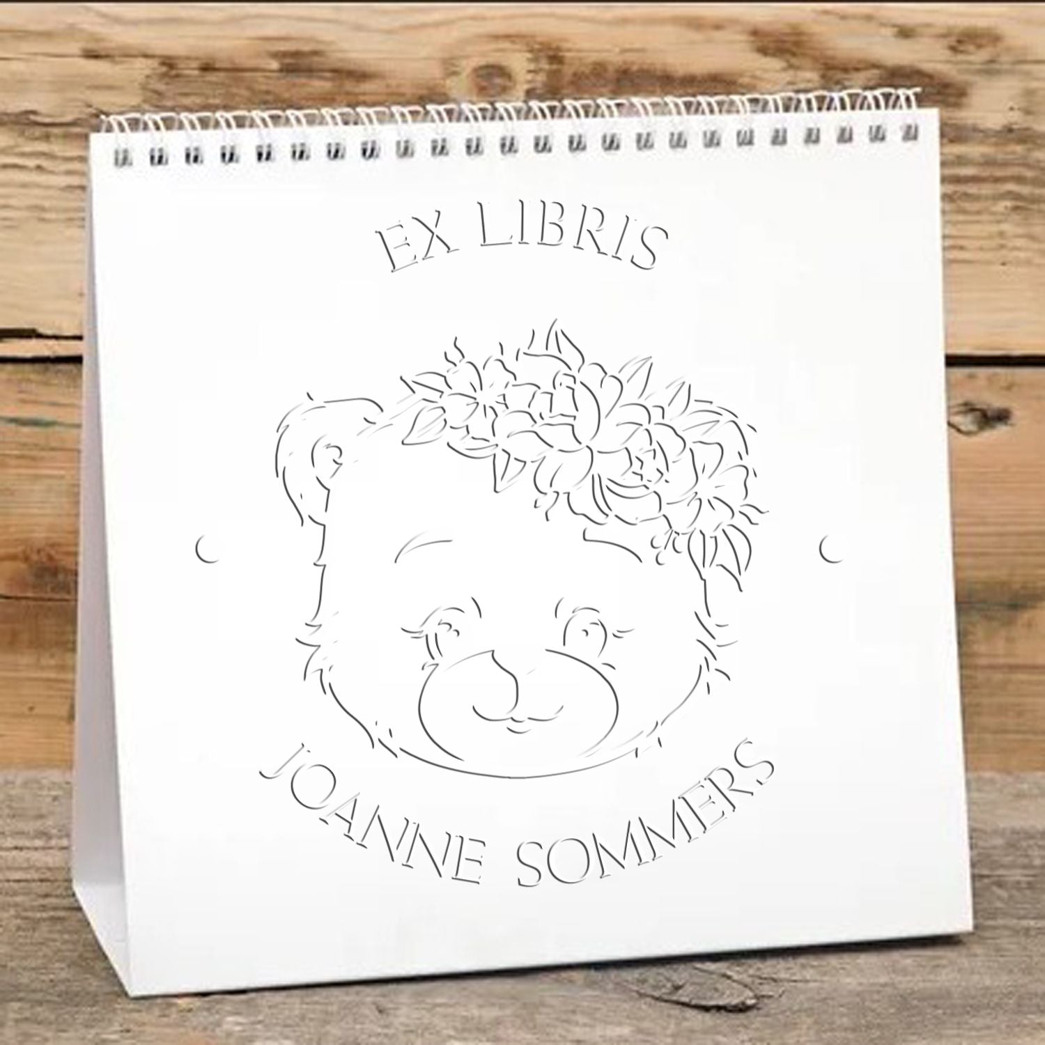 White ex libris stamp seal on a white spiral-bound bag, featuring a bear with floral crown and Joanne Sommers text.