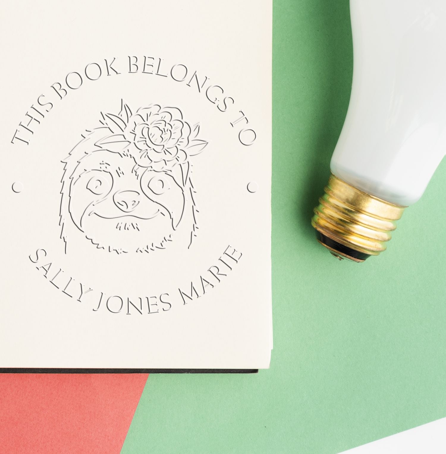Personalized book stamp and seal with sloth floral design on white paper, beside a white-and-gold stamper on mint green background.
