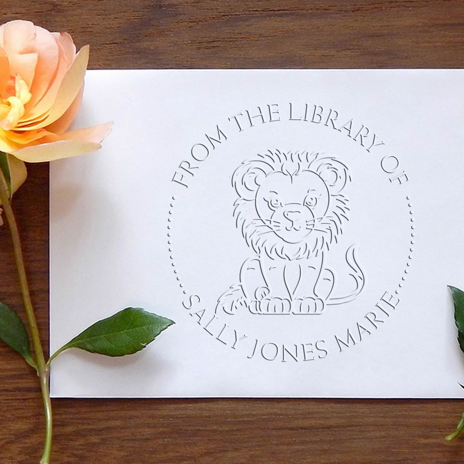 White embossed library stamp and seal with lion crest, peach flower, green leaves, on a dark wood background.