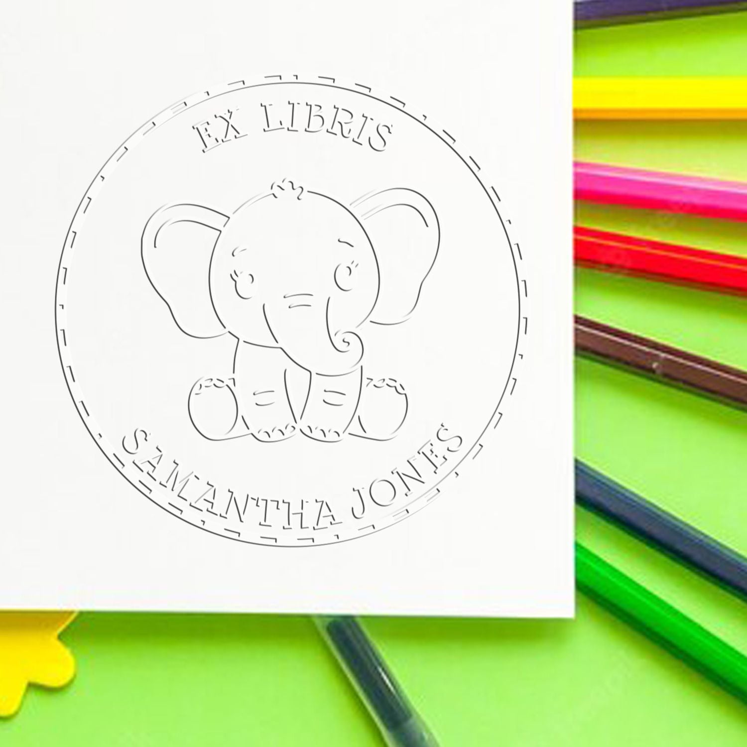 Custom circular stamp seal with elephant outline and EX LIBRIS text on white, against bright neon pencils.