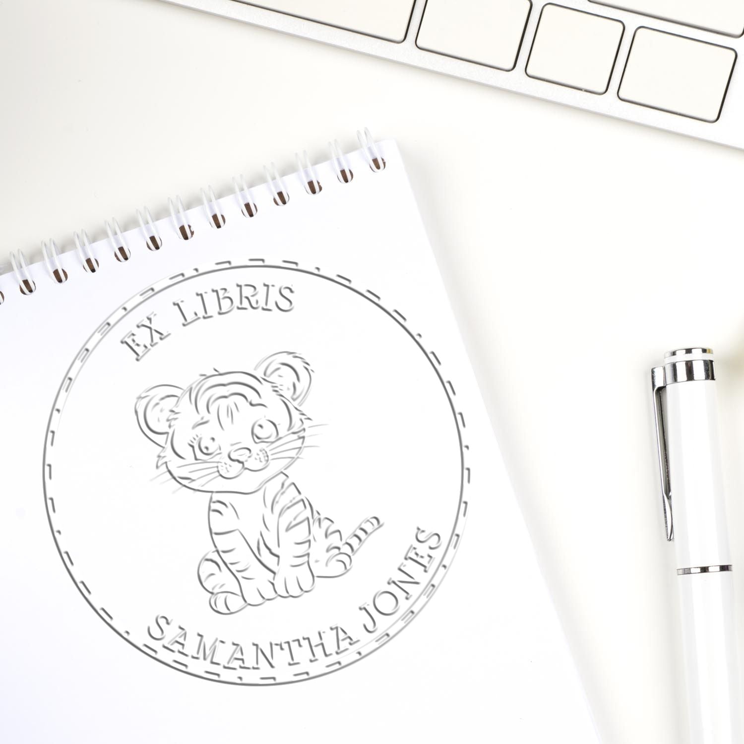 Custom round bookplate stamp seal on white notebook, featuring a tiger and Samantha Jones, with a white pen and keyboard.