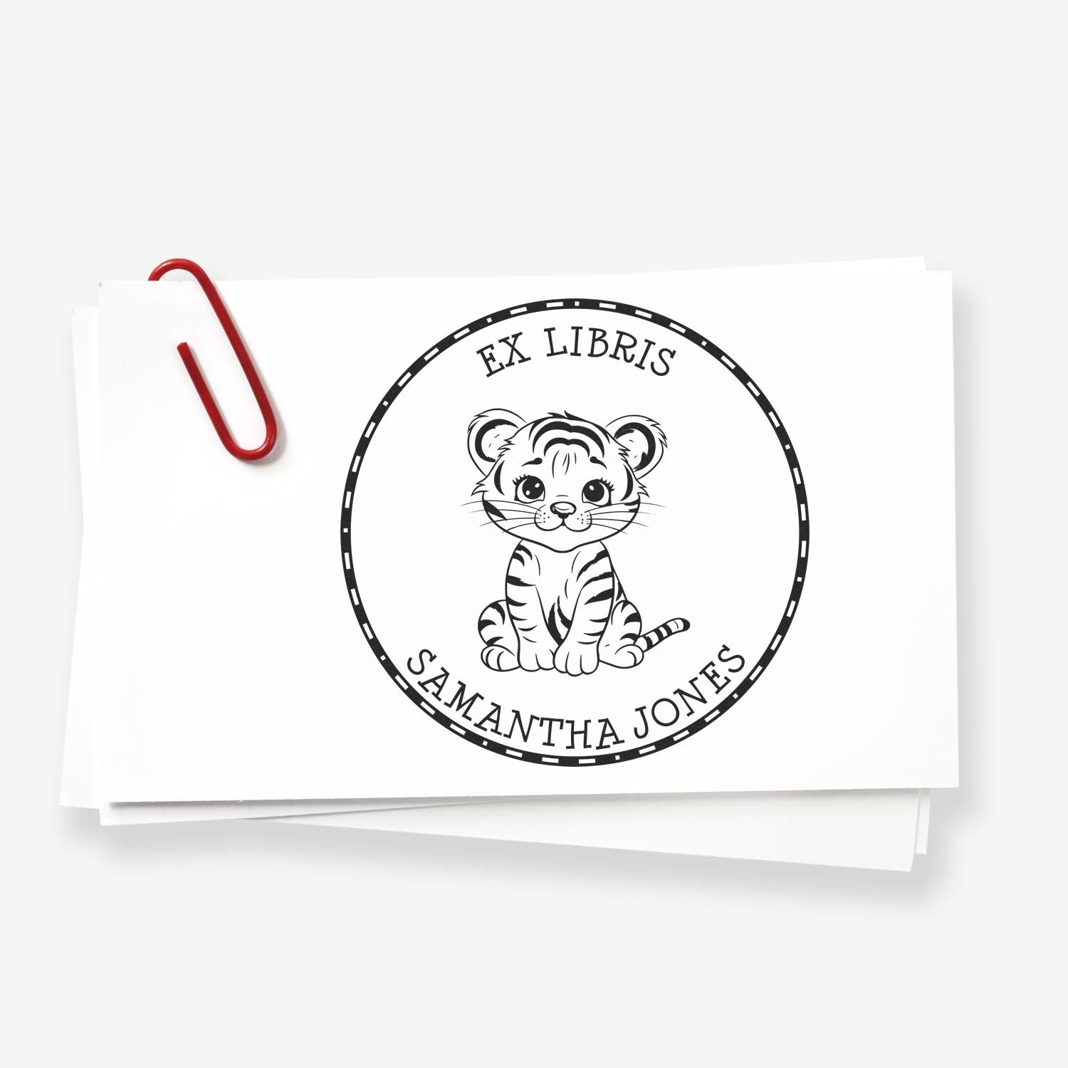 White custom ex libris stamp seal with tiger cub, Samantha Jones text, and red paperclip on stacked cards.