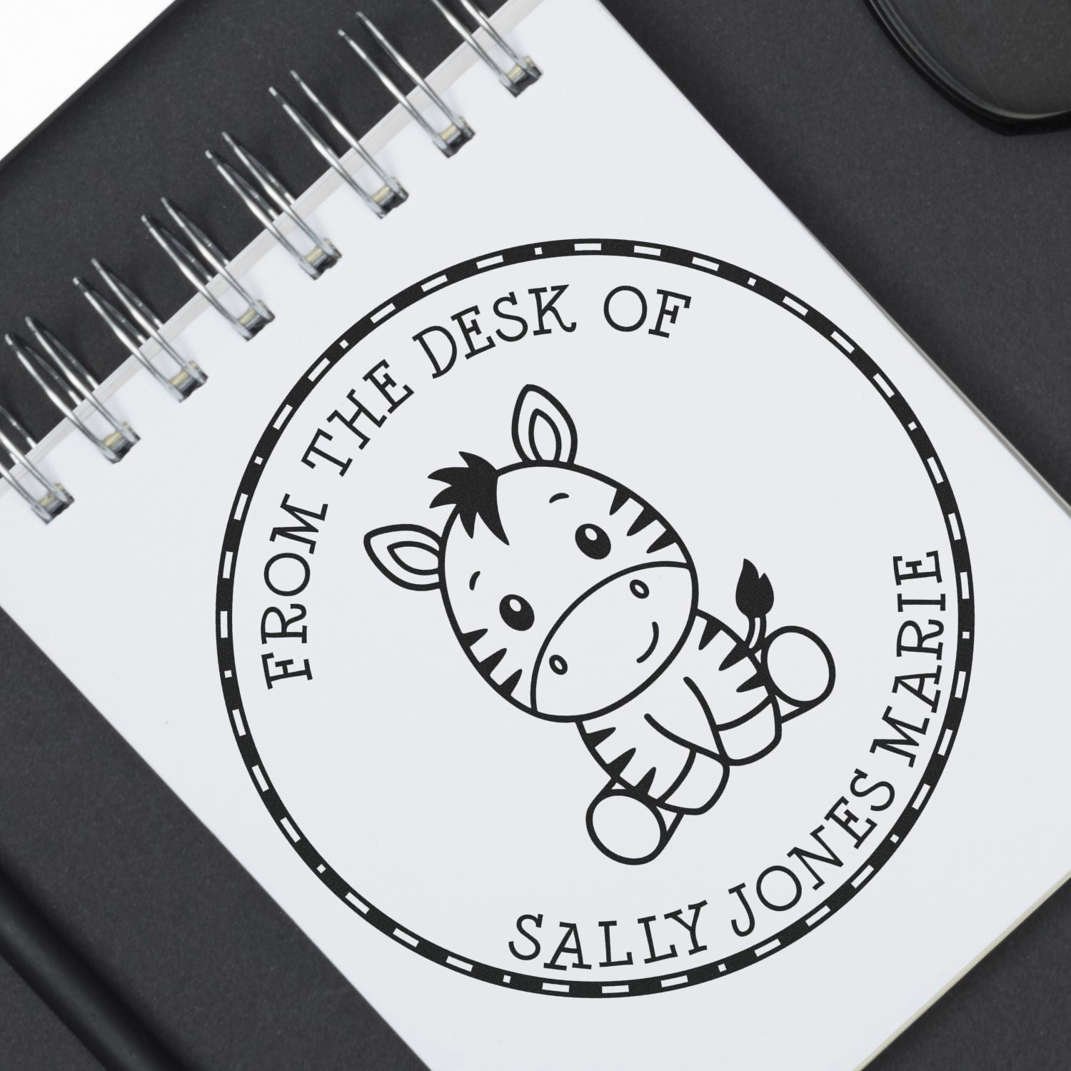 Black-and-white custom stamp seal on a spiral notebook, featuring a zebra and From the Desk of Sally Jones text.