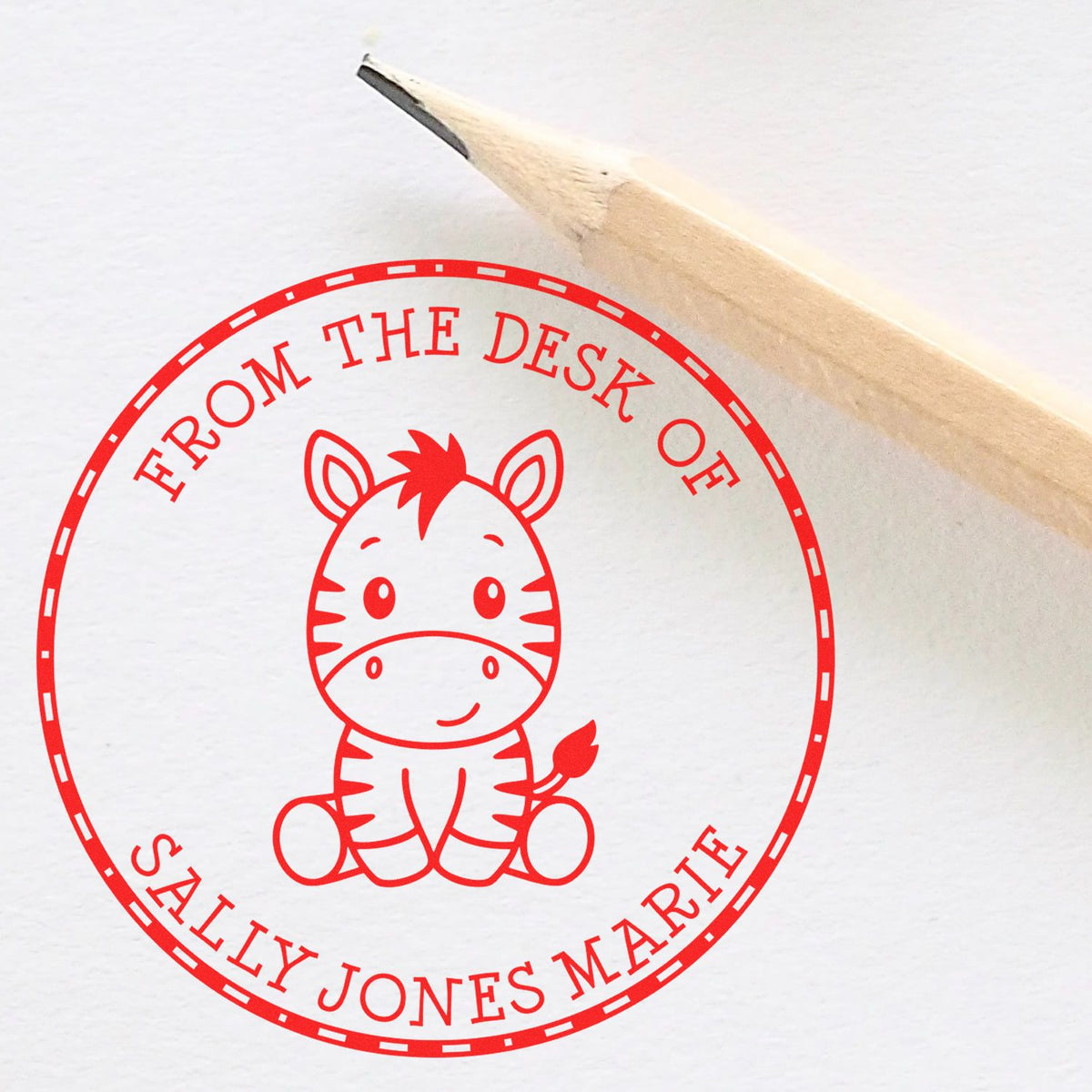 Red circular desk stamp seal with zebra illustration and From the Desk of Sally Jones Marie beside a pencil on white paper
