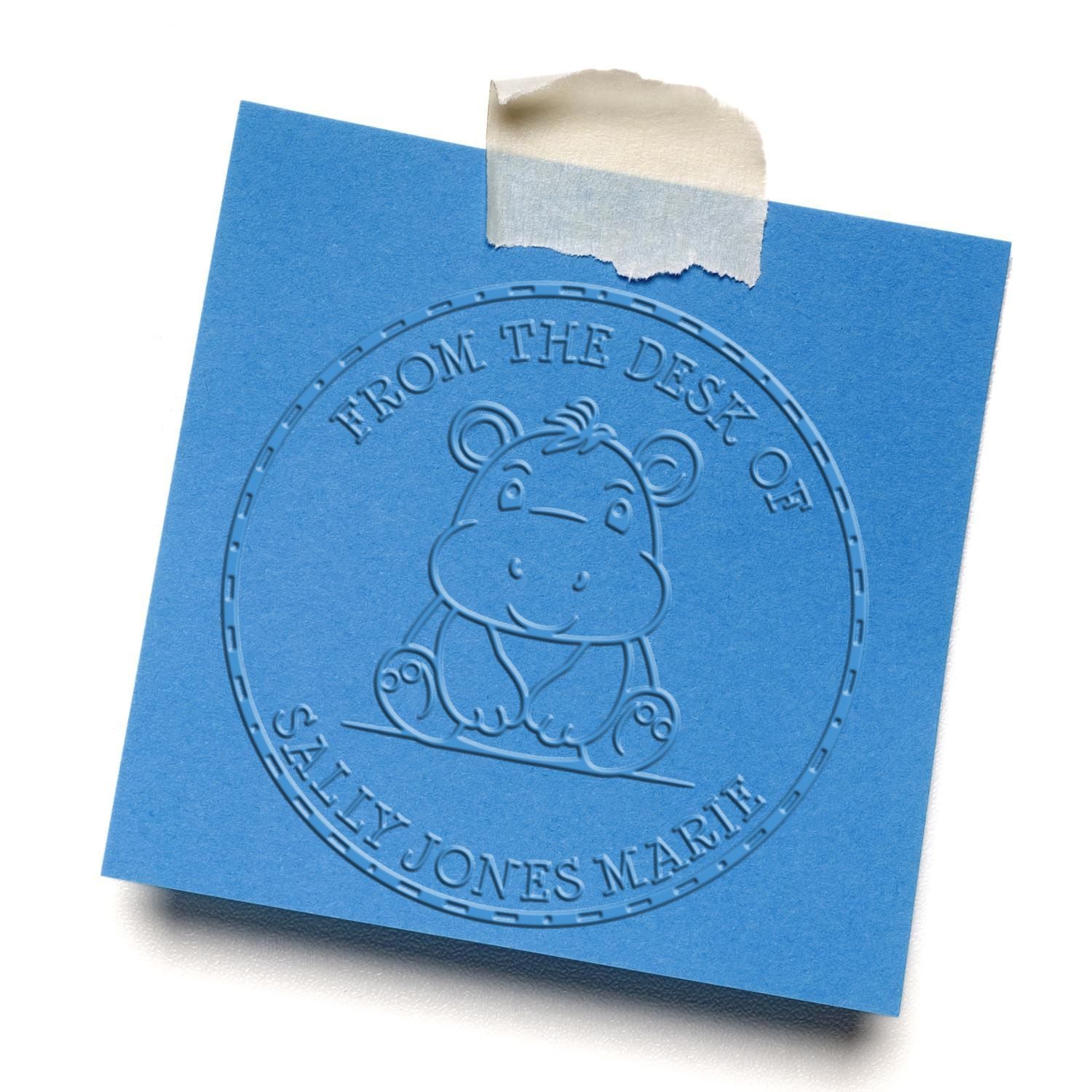 Blue embossed desk seal stamp on square paper, featuring a cartoon hippo and From the Desk of Sally Jones Marie text.