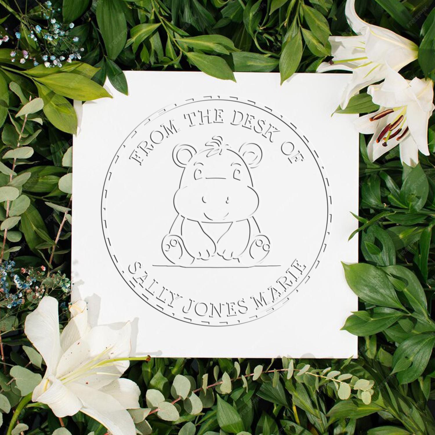 White custom desk stamp and seal with hippo design on a white card, framed by green leaves and white lilies.