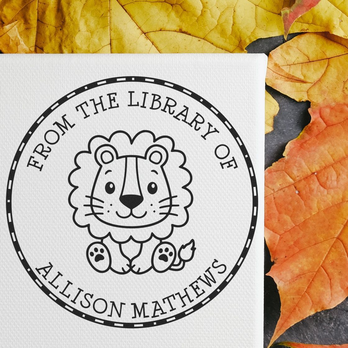 Black circular library stamp seal with lion icon and From the Library of Allison Mathews on white paper, autumn leaves background.