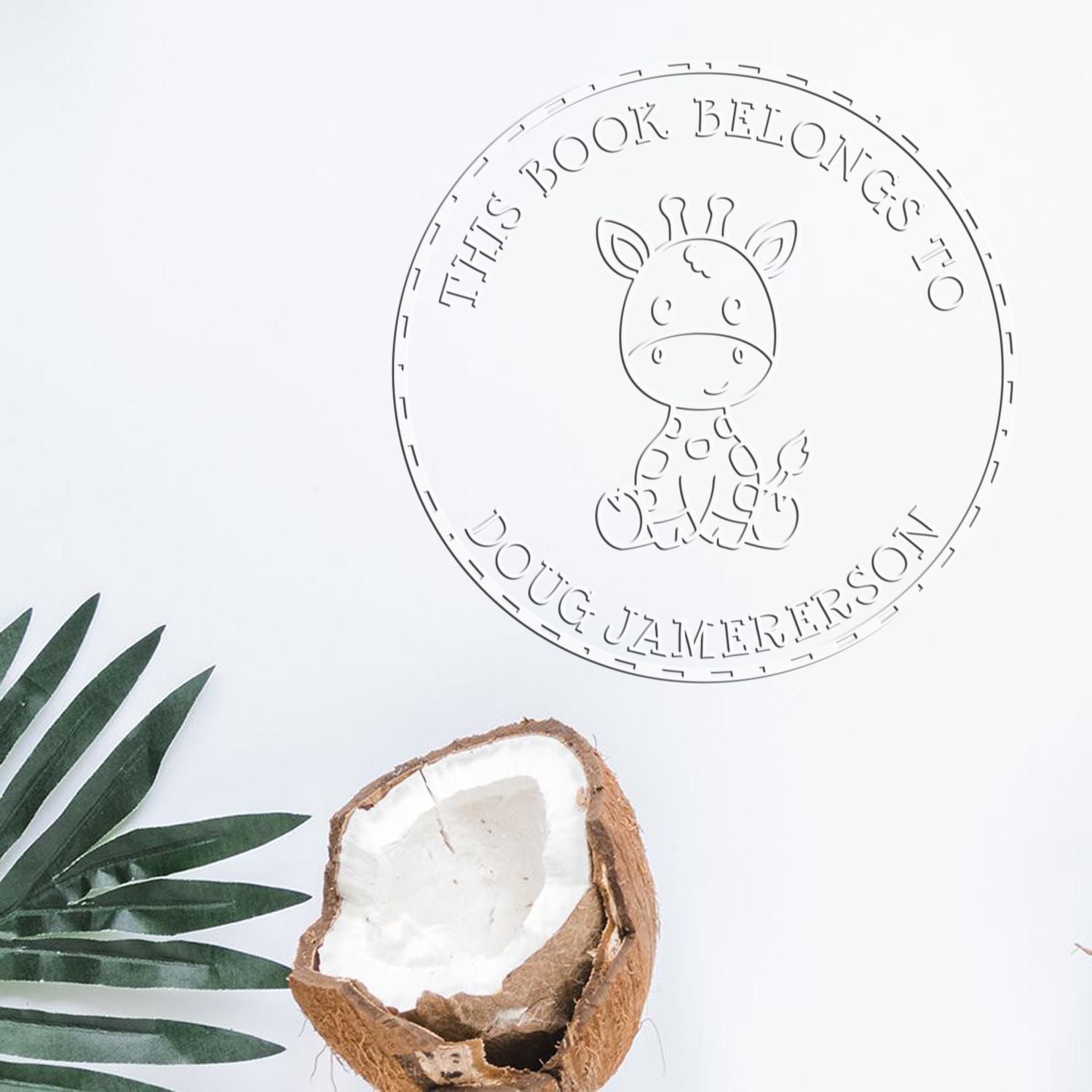 Circular white custom book stamp seal with giraffe and embossed text, on a clean flat lay with green leaves and coconut shell.