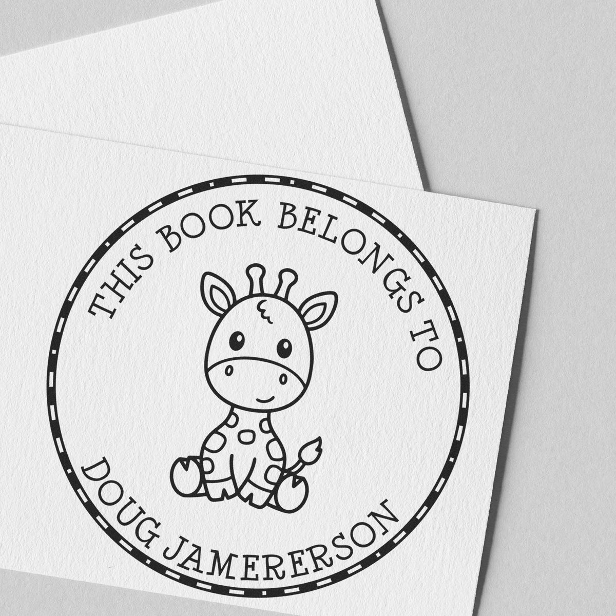 Black custom round book stamp seal with giraffe illustration and This Book Belongs to Doug Jamerson on white paper.