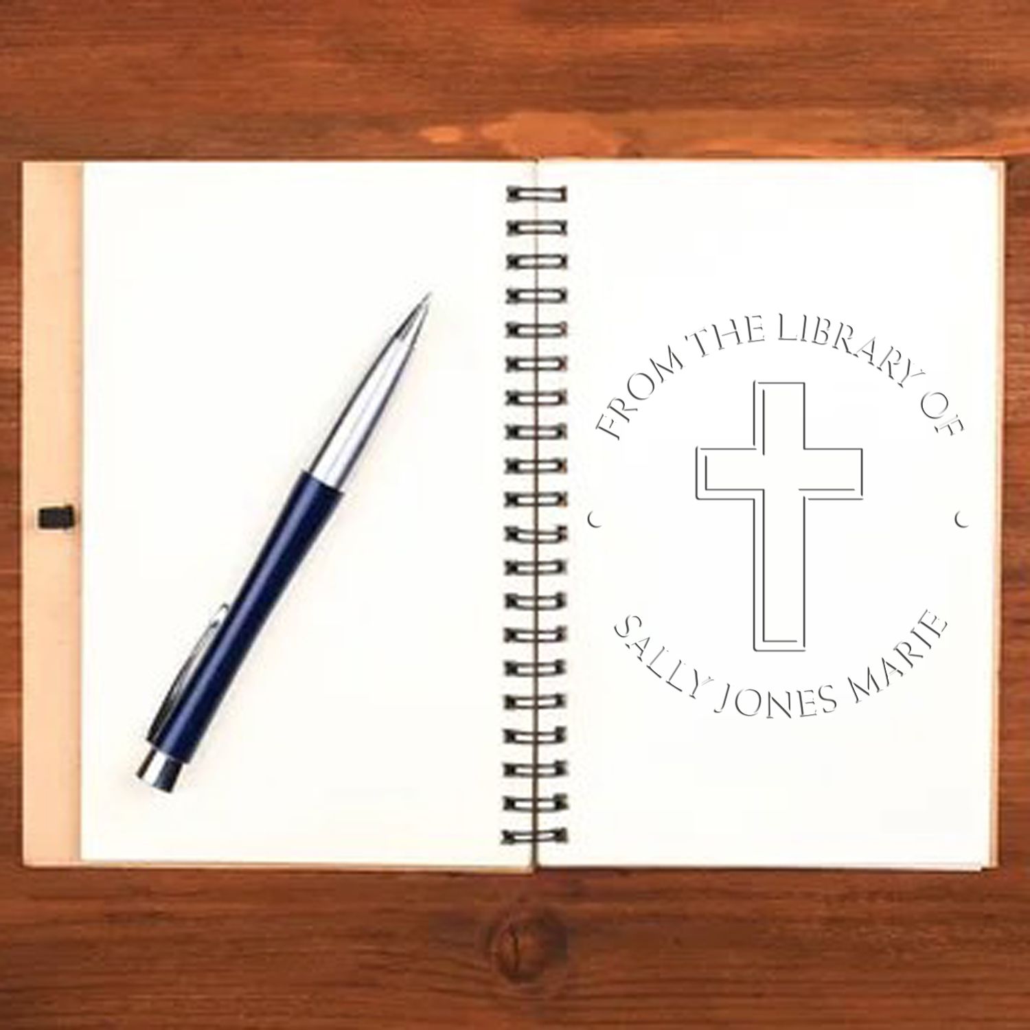 Blue pen beside spiral notebook on wood, showing a custom church stamp seal with cross and Sally Jones Marie text.