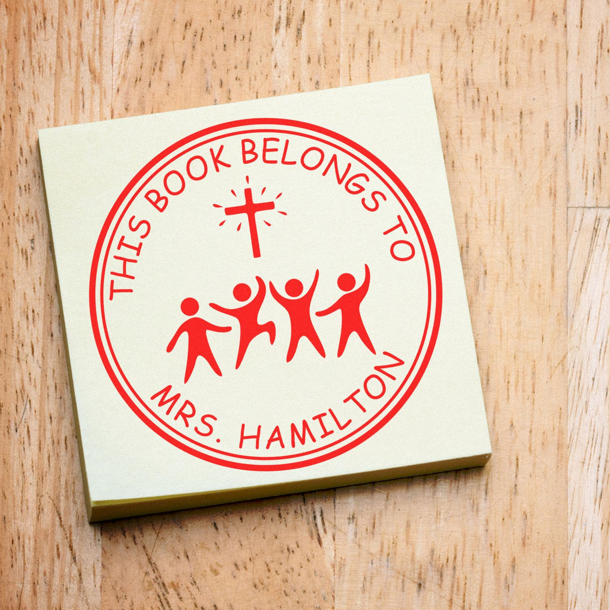 Red custom book stamp/seal on cream square note, reading This Book Belongs to Mrs. Hamilton with cross and figures.