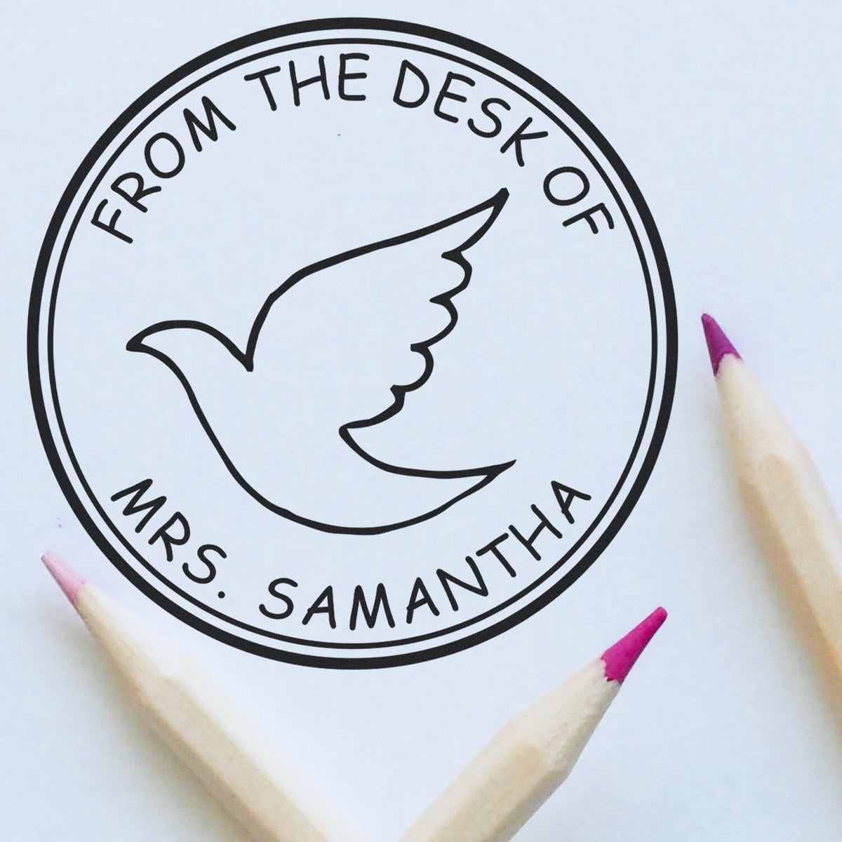 Black circular rubber stamp seal with dove design and From the Desk of Mrs. Samantha on white, framed by pink-tipped pencils