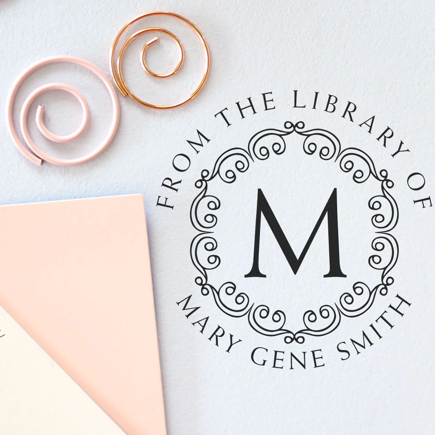Personalized library stamp and wax seal set with black monogram M, blush pink and gold sealing wires, and pale pink paper.