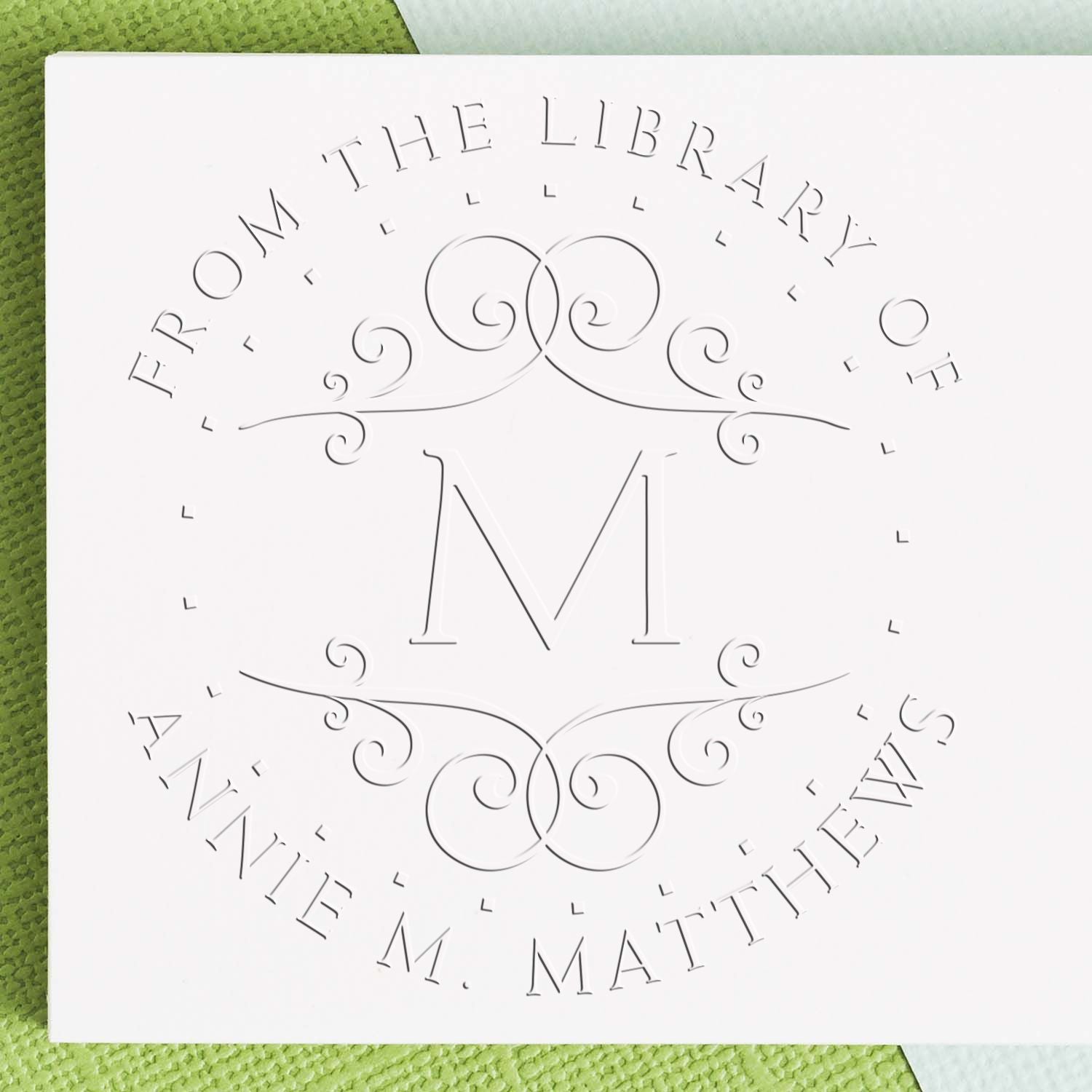 White embossed library stamp seal with ornate M monogram and circular From the Library of M. Matthews text.