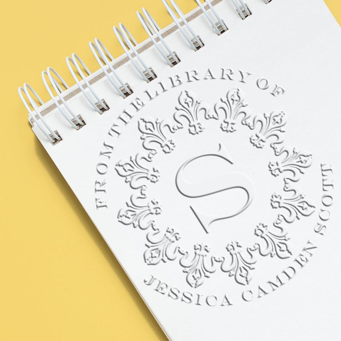 Shiny soft, bold initial custom library paper embosser in use, creating an embossed initial on paper for personalized library branding.