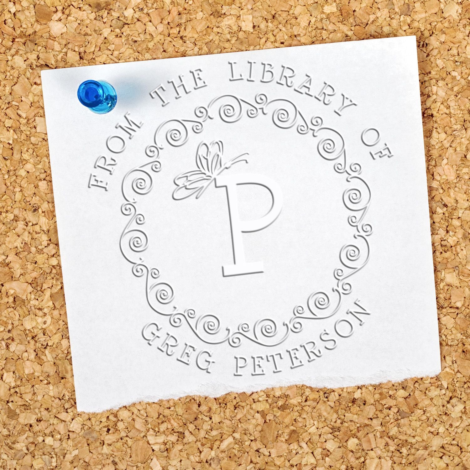 White embossed custom library stamp and seal on tan cork, with a blue wax seal and ornate letter P.