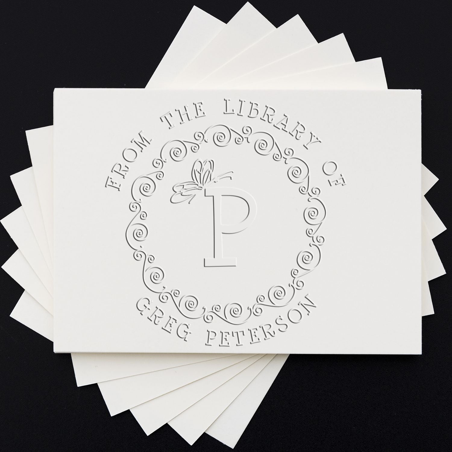 Stacked white stamp and seal product samples with embossed P monogram, swirl border, on a black background.