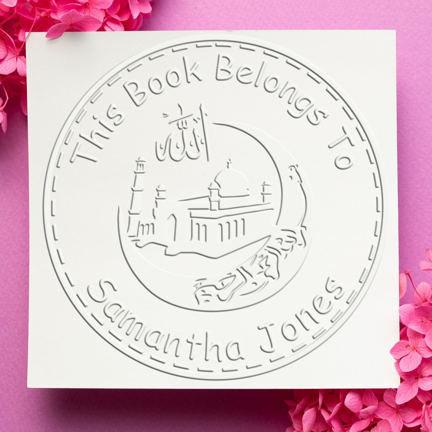 White embossed circular book stamp seal reading This Book Belongs To Samantha Jones on a pink floral background.
