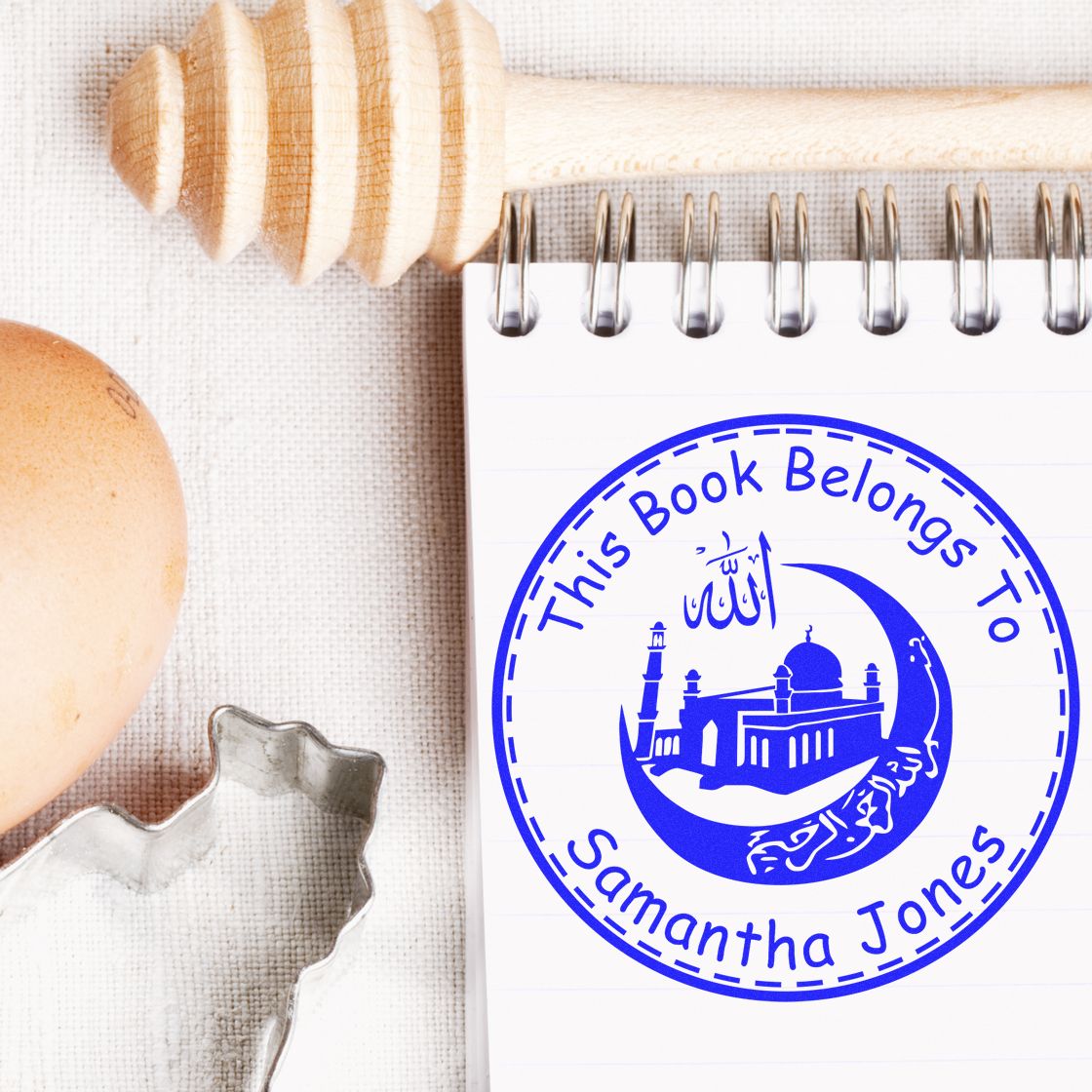 Blue custom book-belongs stamp seal on a white notepad, beside a wooden stamp, egg, and cookie cutter.