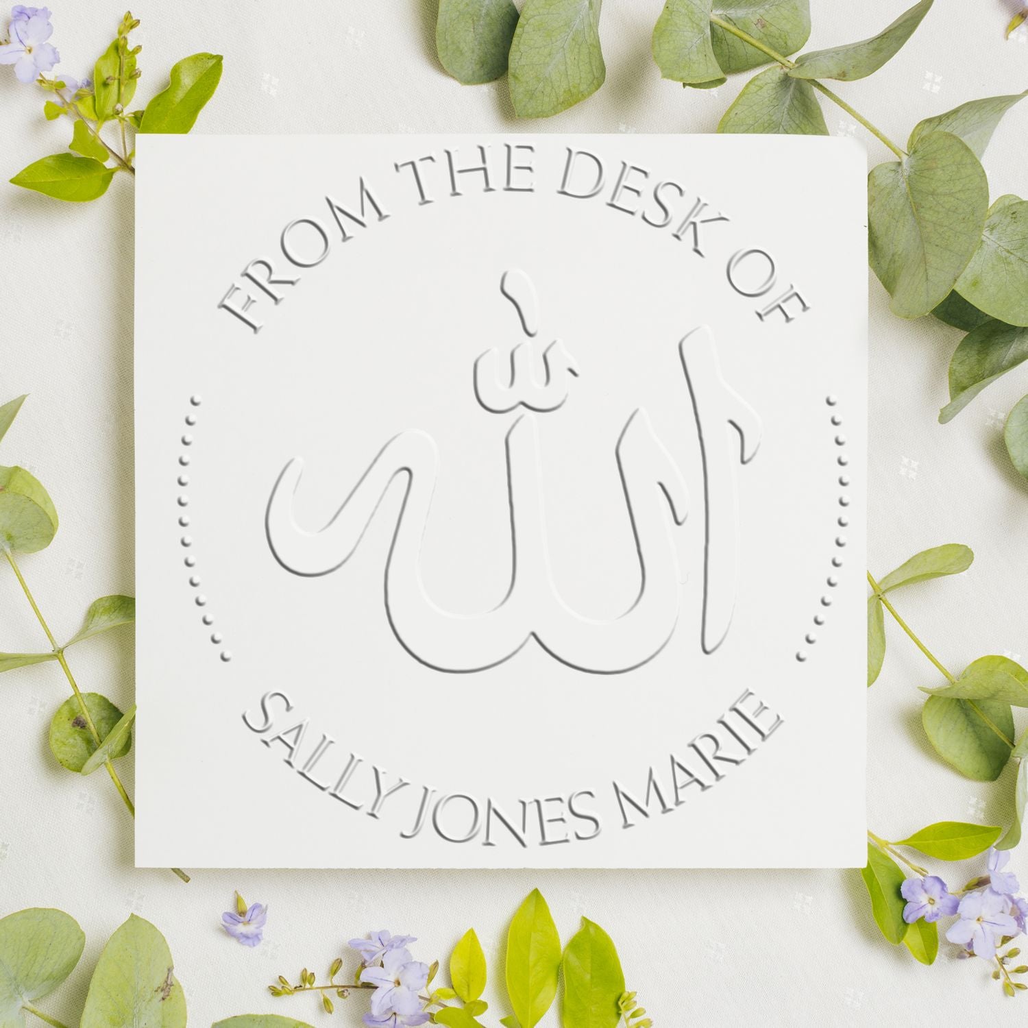 White custom stamp seal with gray embossed Arabic calligraphy and names, framed by green leaves and purple flowers.