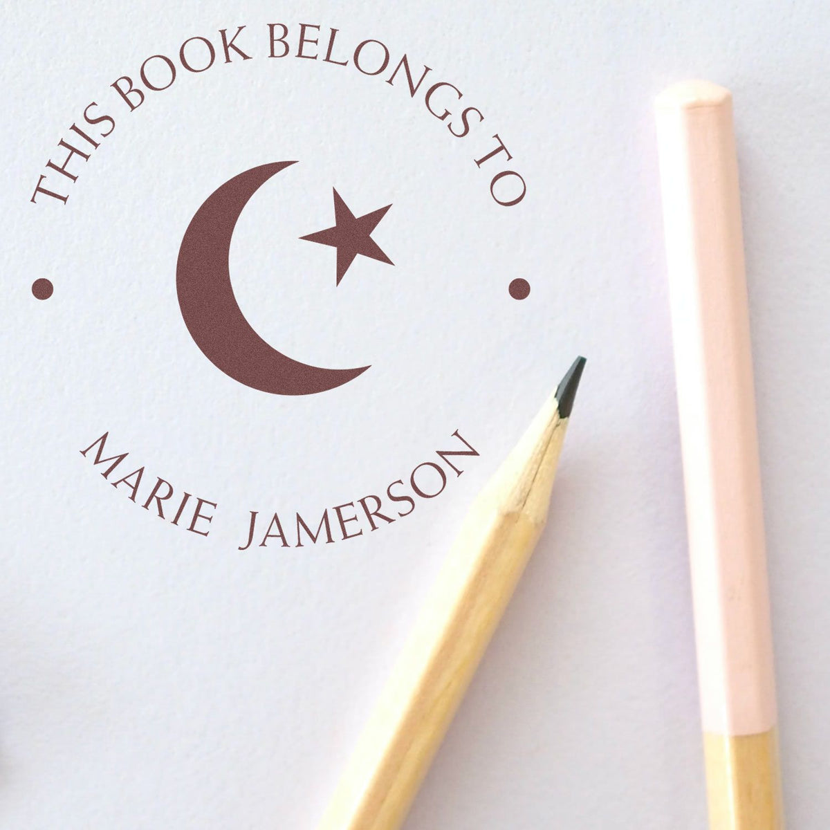 Brown personalized book stamp and seal with crescent-star emblem and This Book Belongs to Marie Jamerson on white paper
