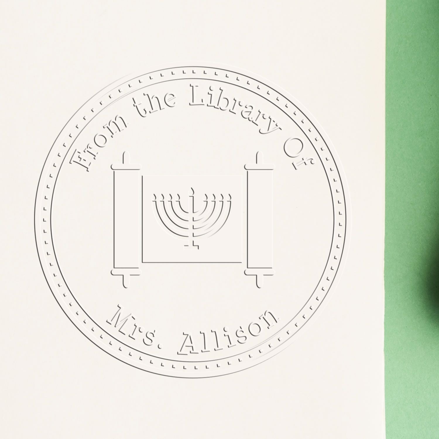 Embossed circular library stamp seal in gray on white paper, reading From the Library of Mrs. Allison, with a menorah design and green edge.