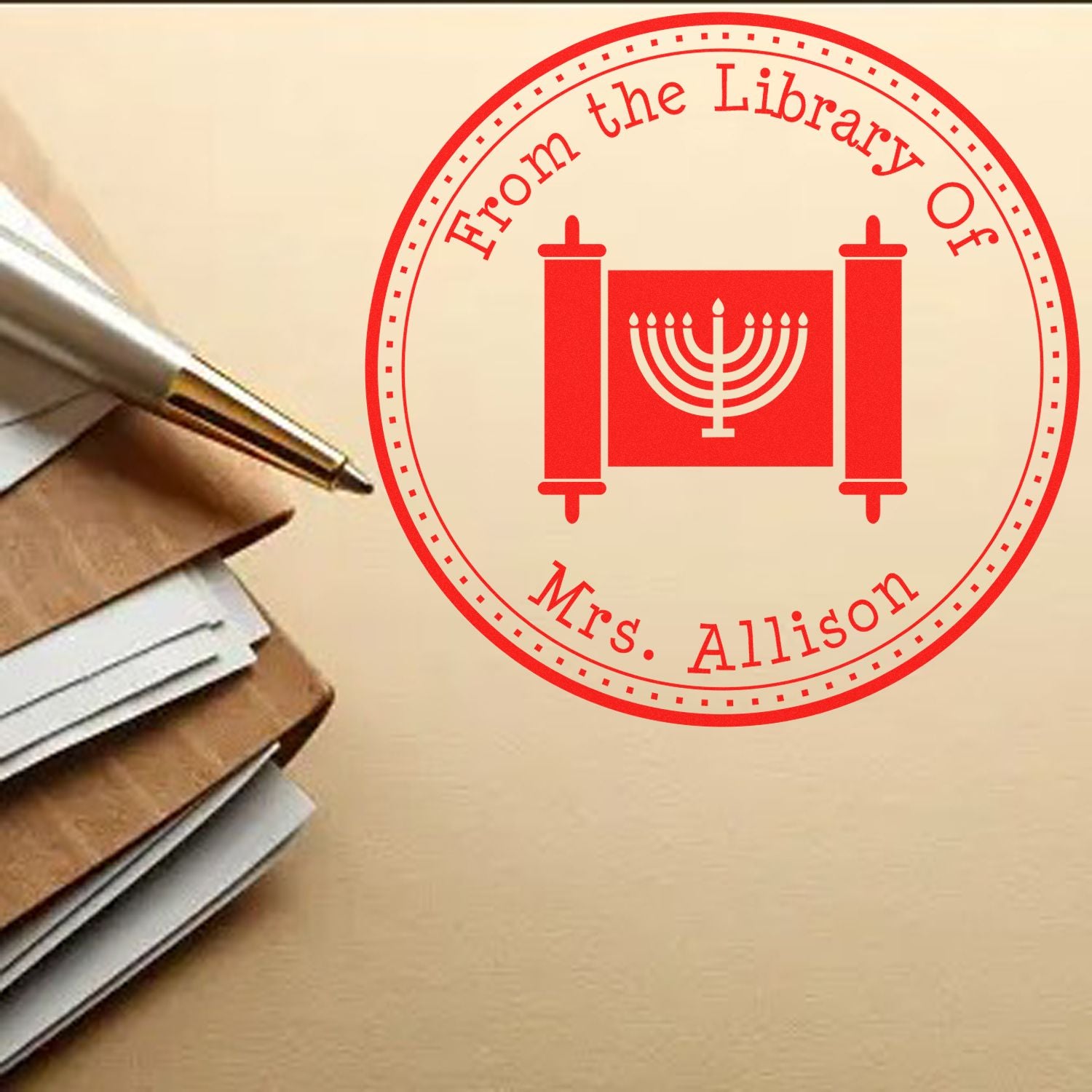 Red custom library seal stamp with menorah emblem and Mrs. Allison text beside a pen and stacked envelopes.