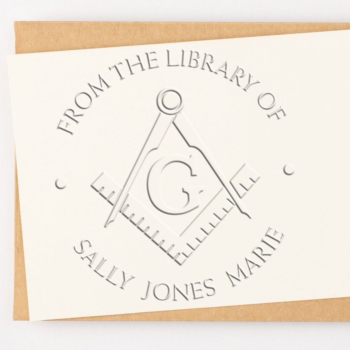 Embossed white library stamp seal with gray compass design and From the Library of Sally Jones Marie on tan card