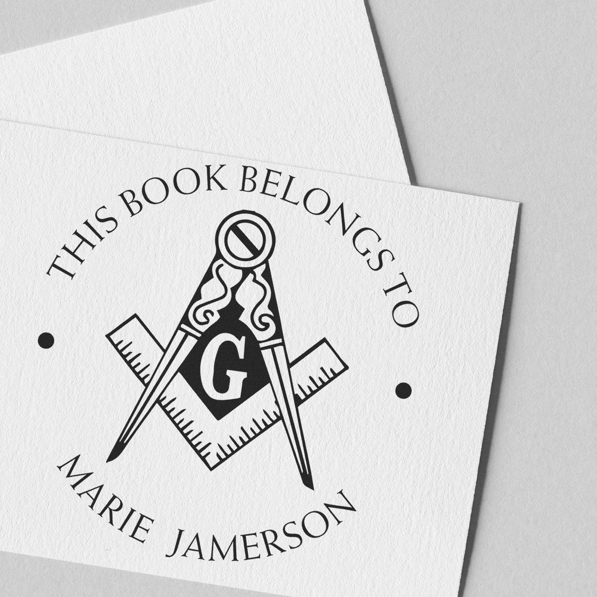 Black custom book stamp and seal with compass, letter G, and This Book Belongs To Marie Jamerson on white paper.