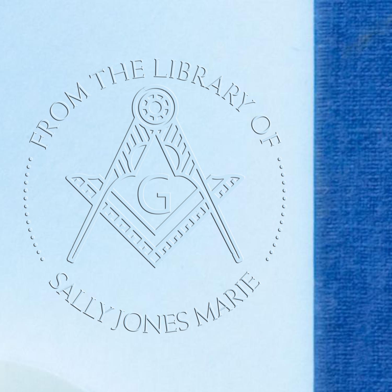 Embossed light blue library seal with compass-and-G emblem and Sally Jones Marie text beside a blue cloth edge.