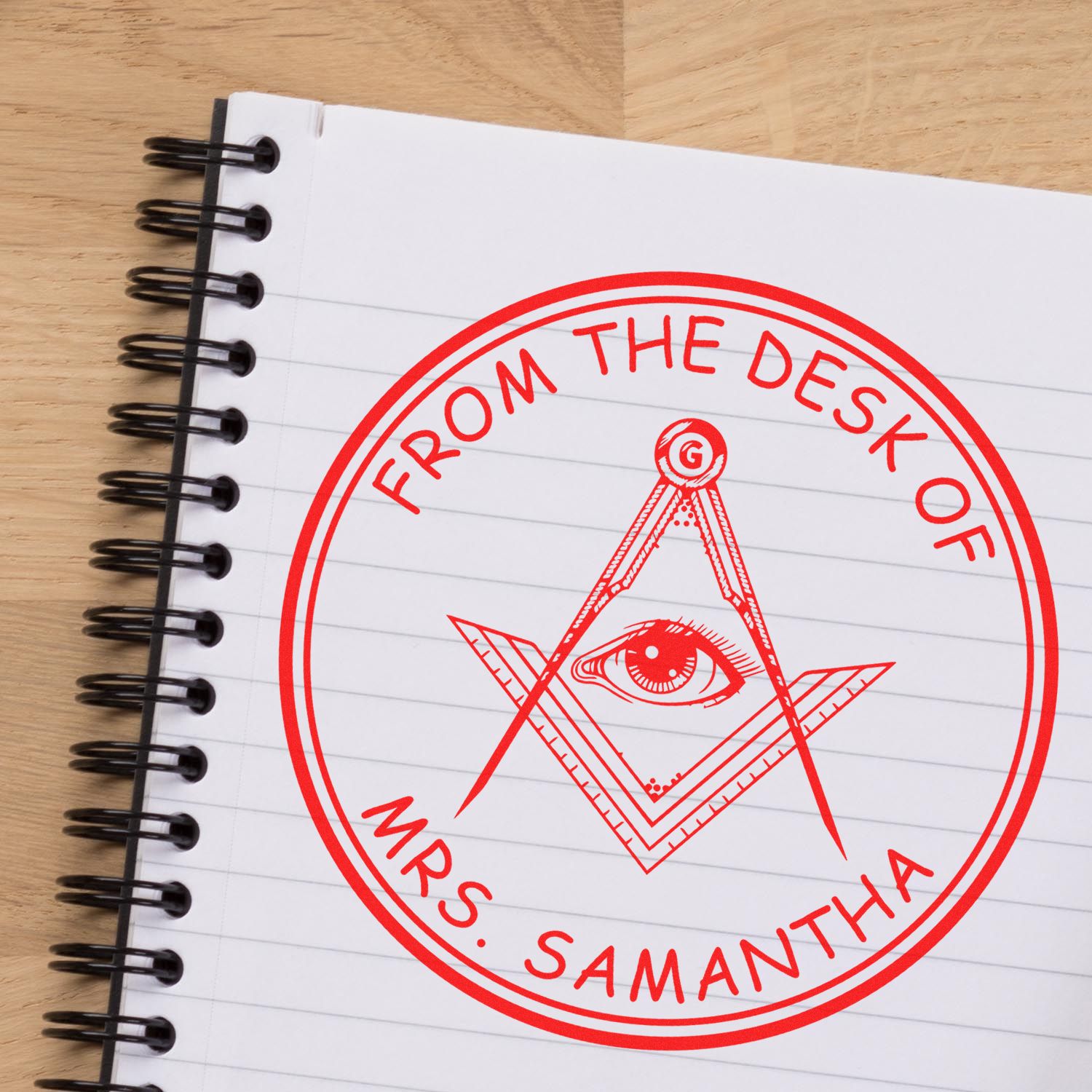 Red circular desk stamp and seal on a white spiral notebook, featuring an eye symbol and From the Desk of Mrs. Samantha text.
