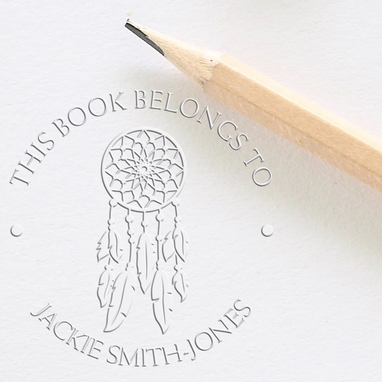 White embossed stamp seal with dreamcatcher, This Book Belongs to Jackie Smith-Jones text, and a beige pencil.