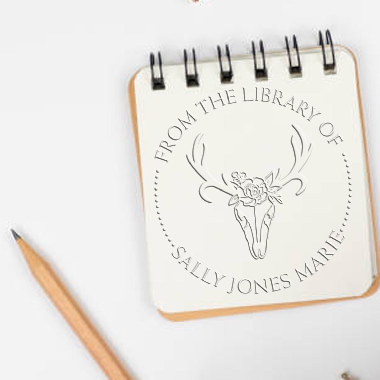 Custom stamp seal on cream spiral notebook with deer skull floral design and From the Library of Sally Jones Marie text