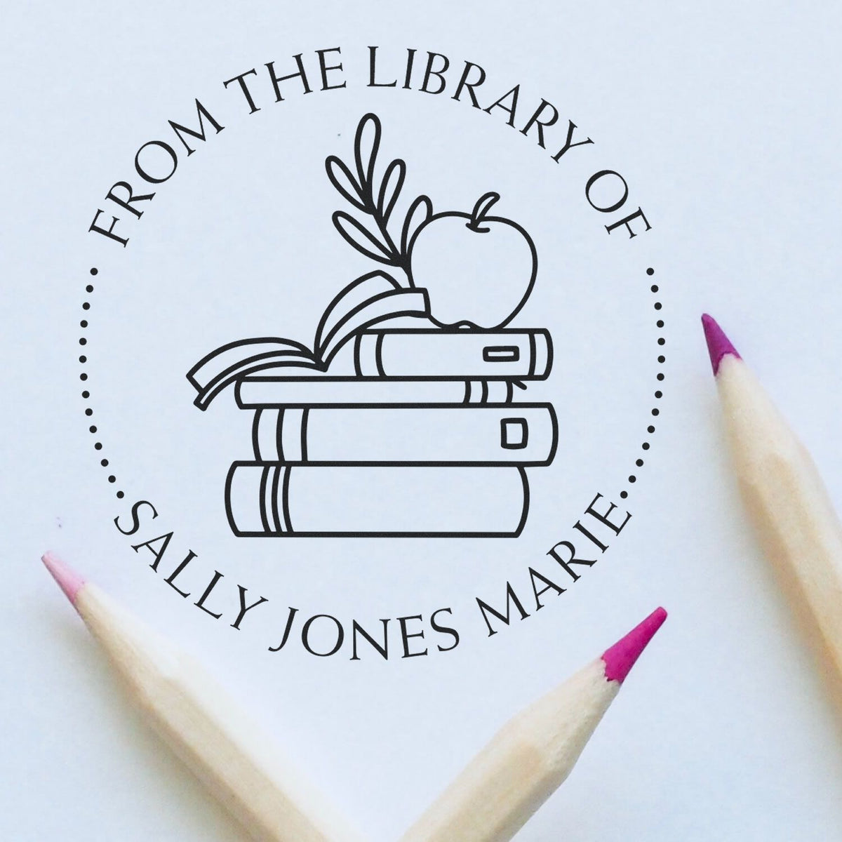 Custom black library stamp and seal with books, apple, and leaves on white, framed by pink pencil tips.