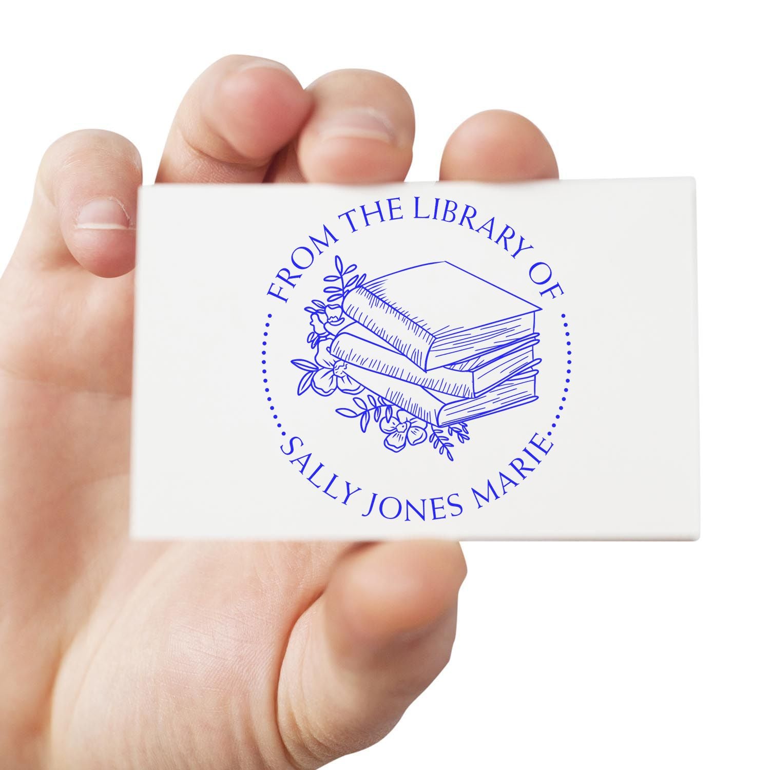Hand holding a white custom stamp seal with blue book stack, floral design, and circular Sally Jones Marie library text.