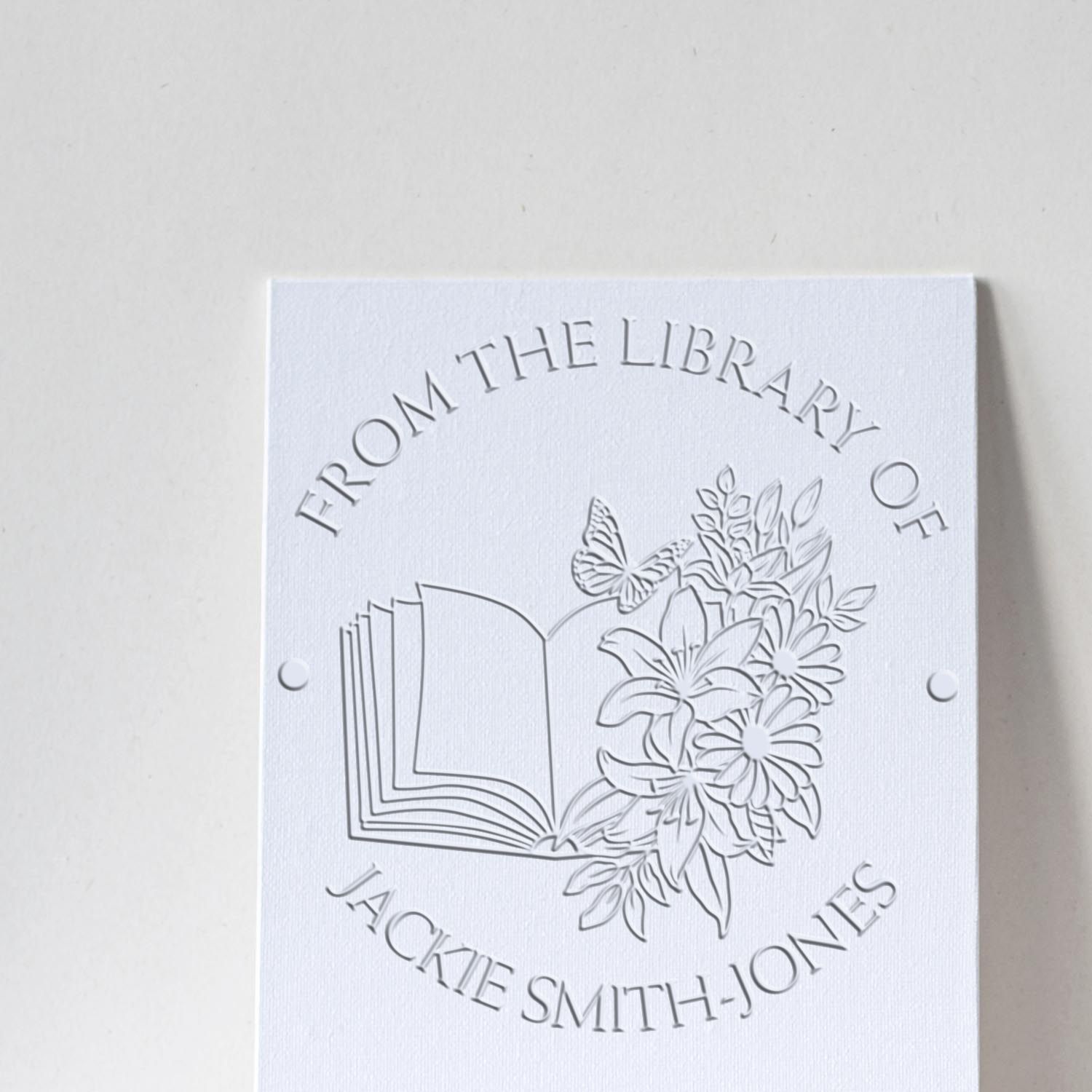White embossed library stamp seal with open book, flowers and butterfly, reading From the Library of Jackie Smith-Jones.