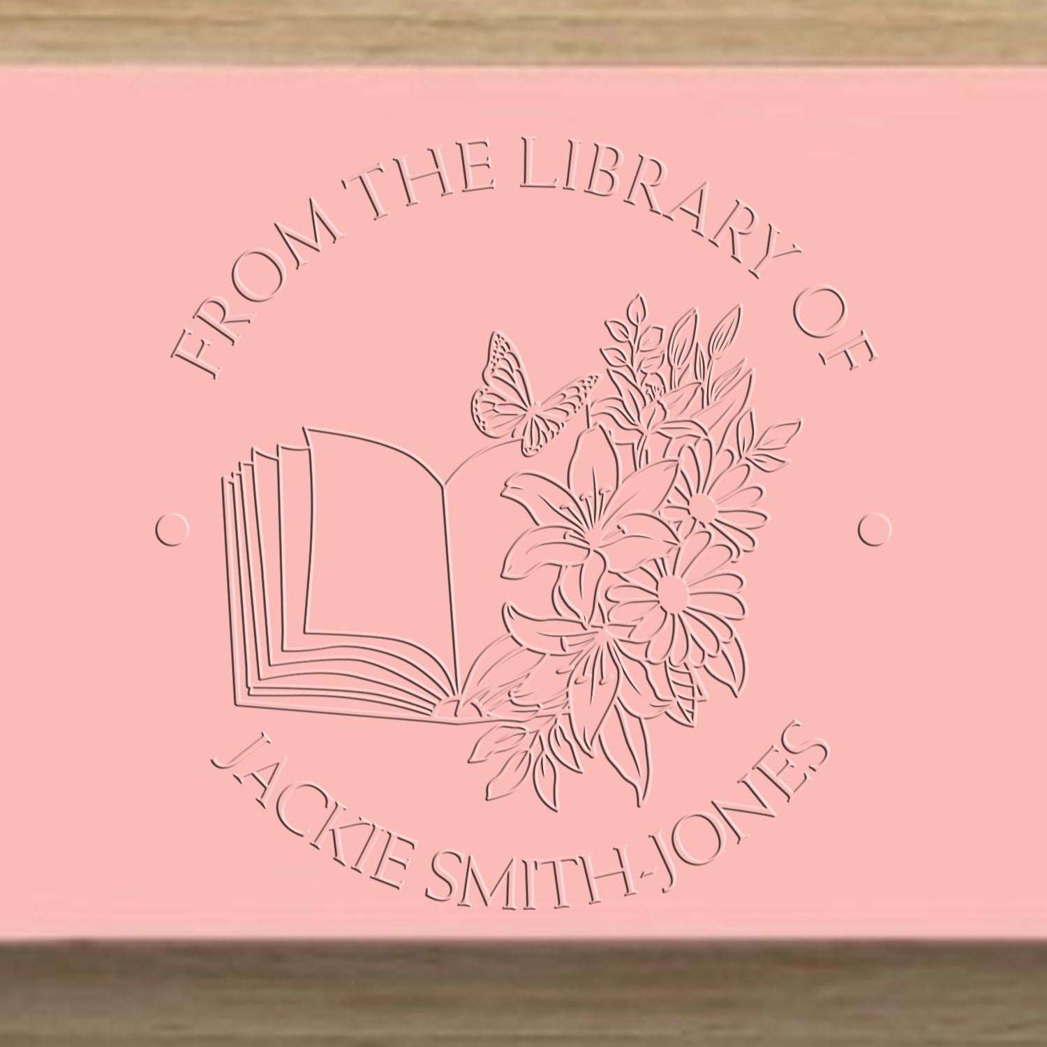 Pink custom library stamp seal with open book, flowers, butterfly, and circular text for Jackie Smith-Jones.