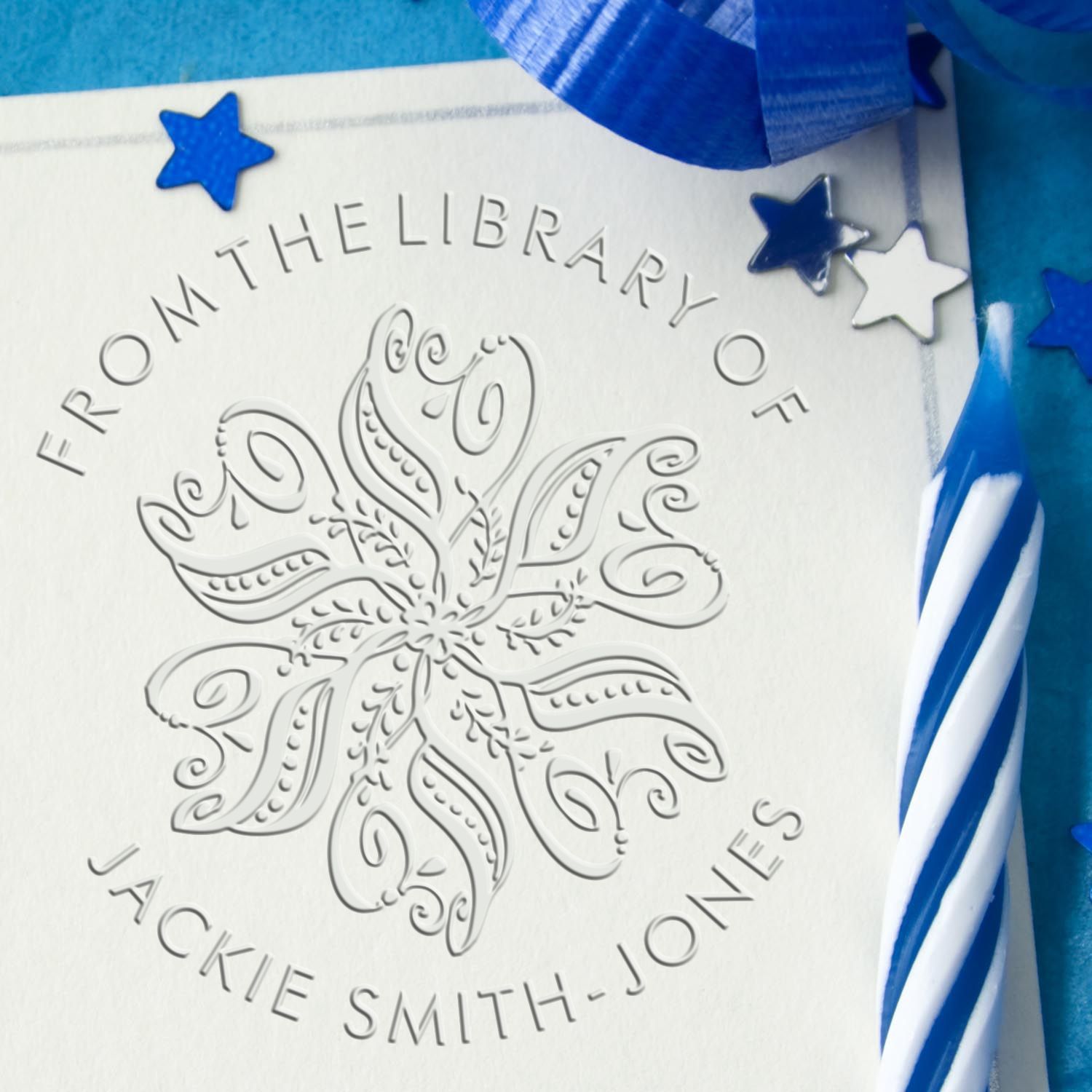 Embossed white library stamp seal with floral design, blue ribbon accents, and star decorations on a blue background.