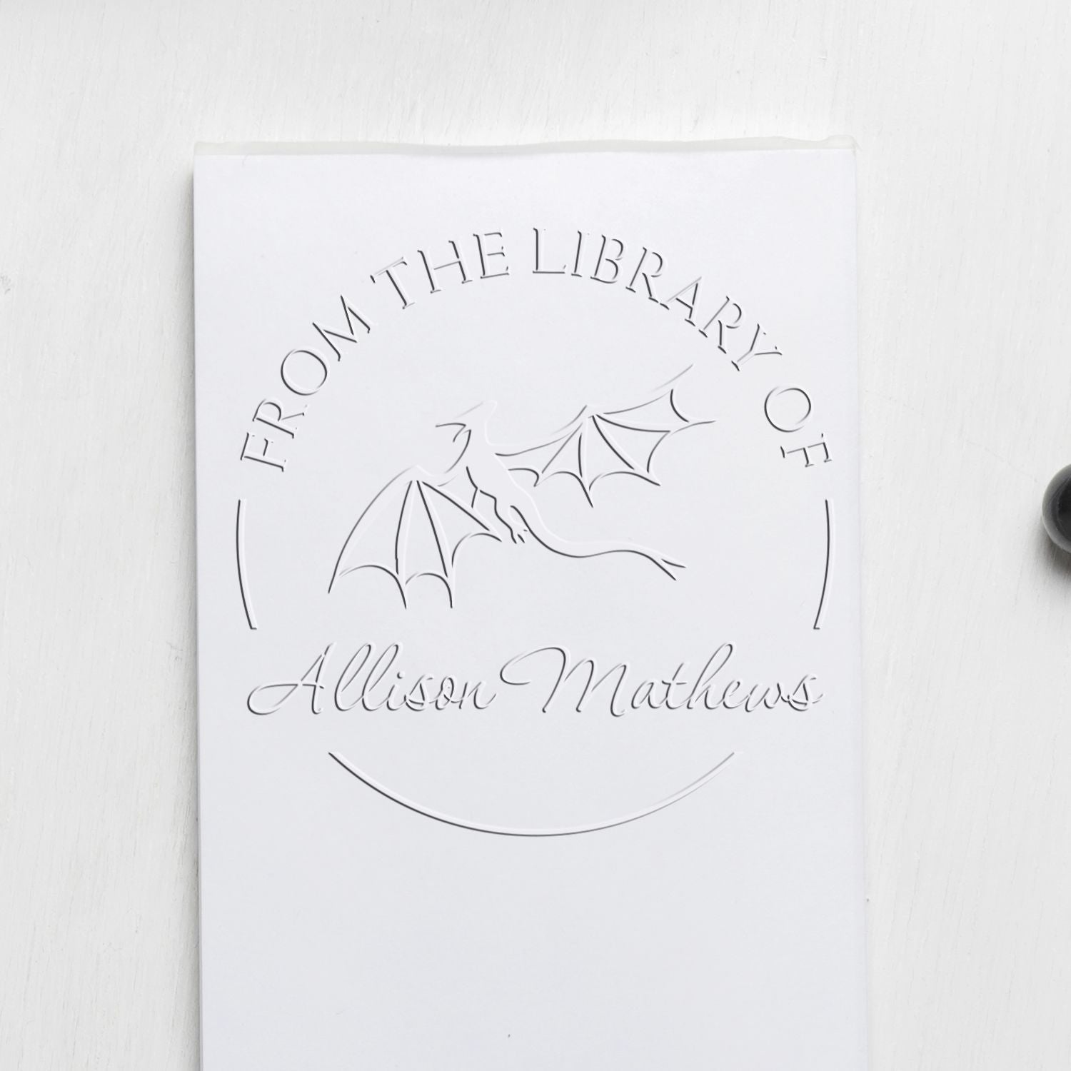 White custom library stamp seal with embossed dragon and From the Library of Allison Mathews text on a white background.