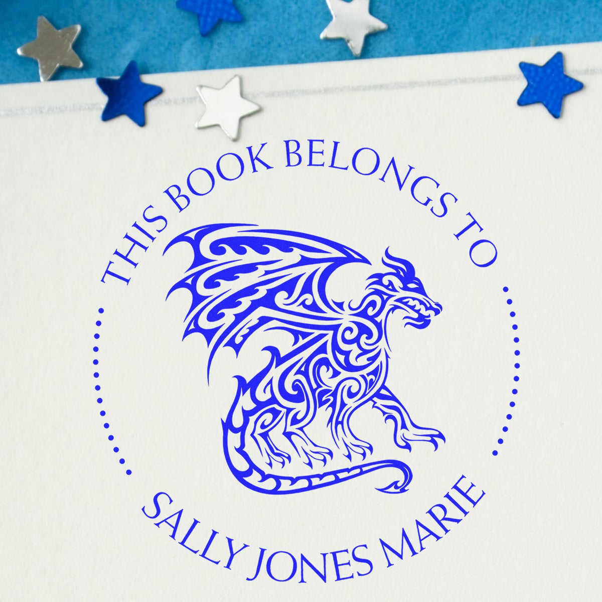 Blue custom book stamp seal with ornate dragon and circular text for Sally Jones Marie on white paper.