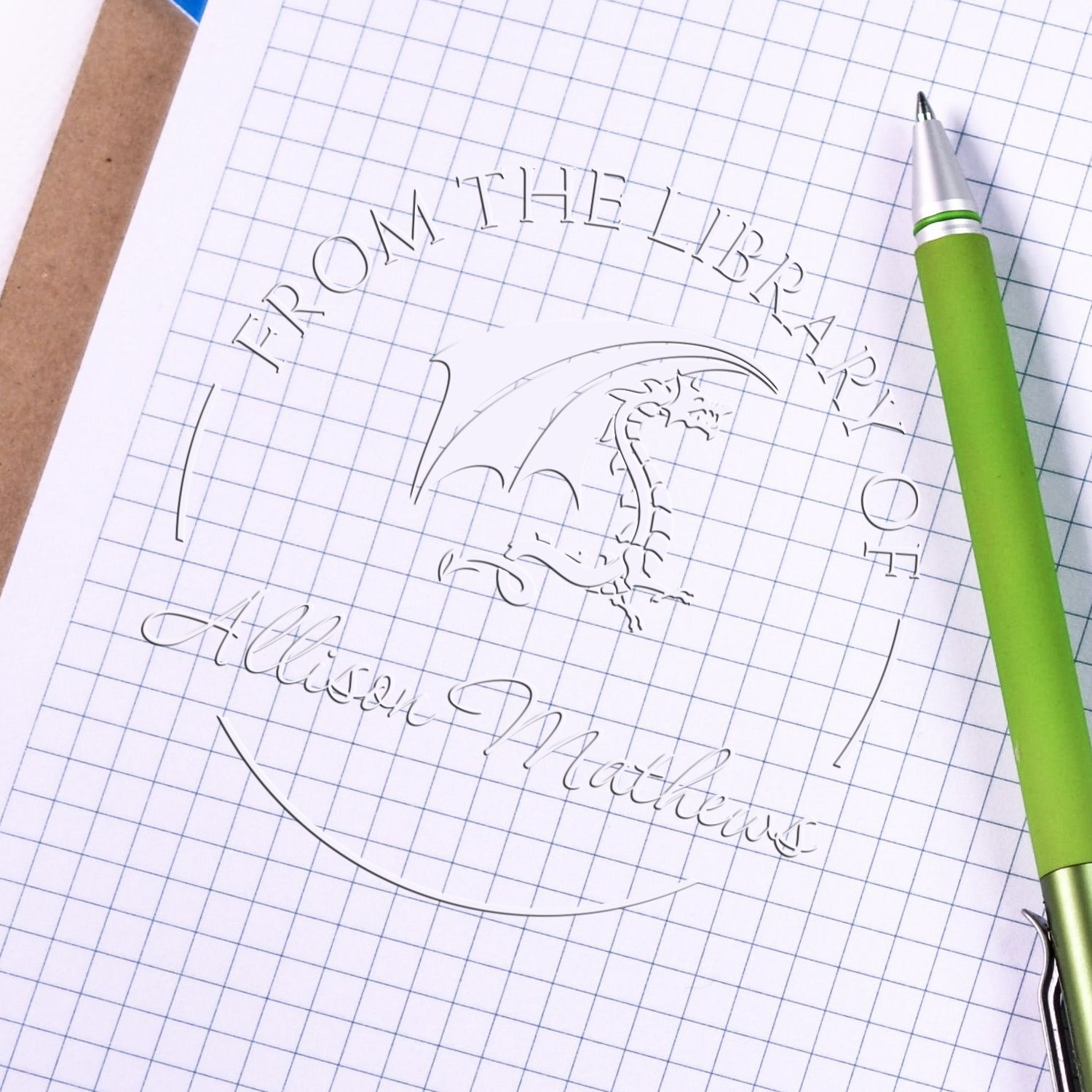 Silver custom stamp and seal with dragon logo on graph paper, beside a green pen