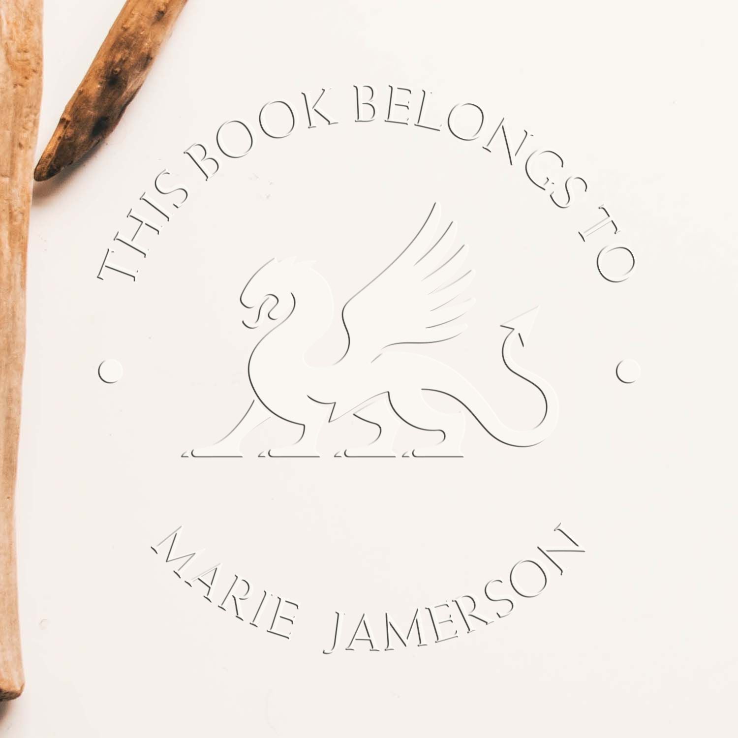 White embossed book-belongs-to stamp seal with swan logo and brown wooden handles, reading This Book Belongs to Marie Jamerson.