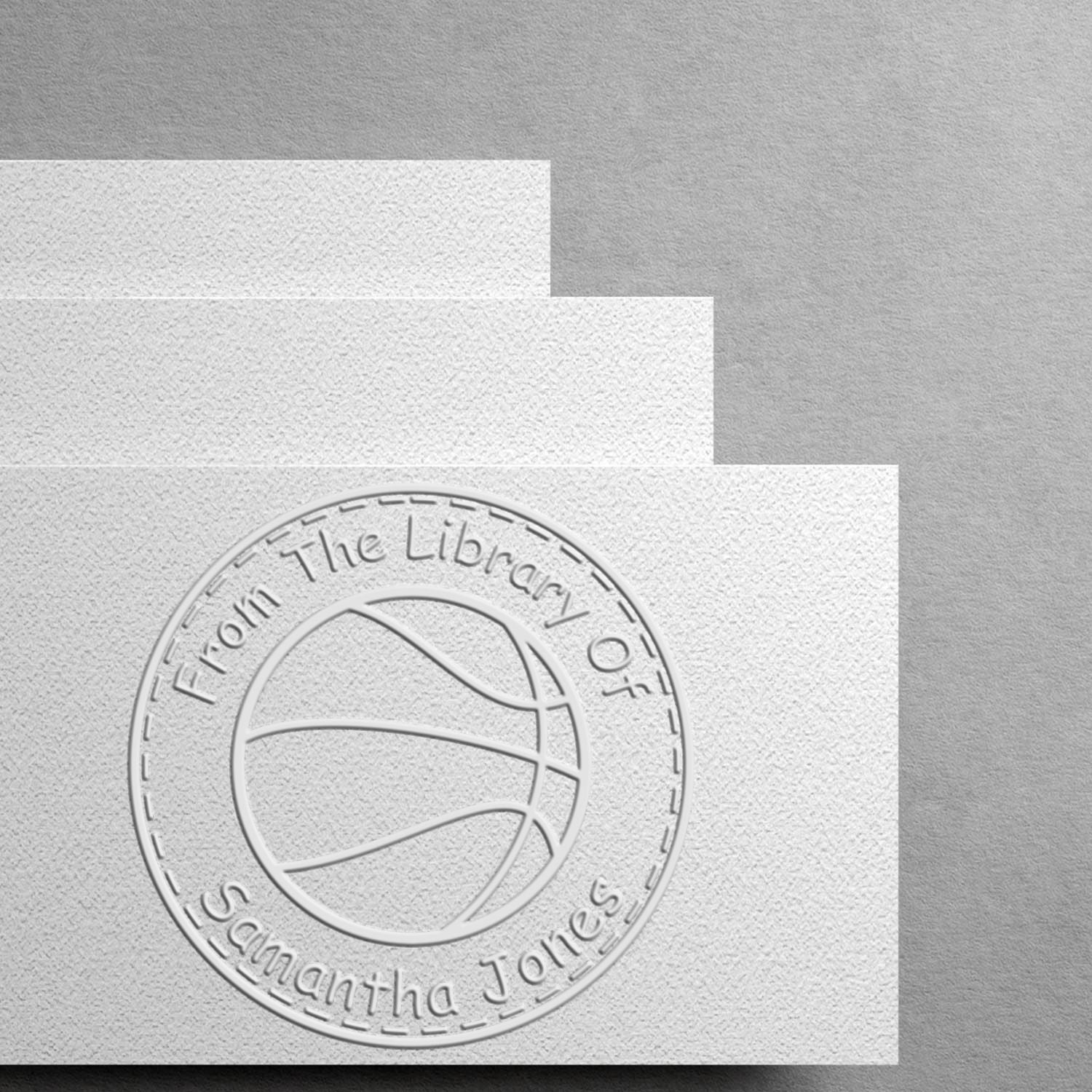 Embossed white custom library stamp seal on textured paper, circular basketball logo and From The Library Of Samantha Jones.